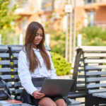Uma garota está sentada em um banco com um laptop